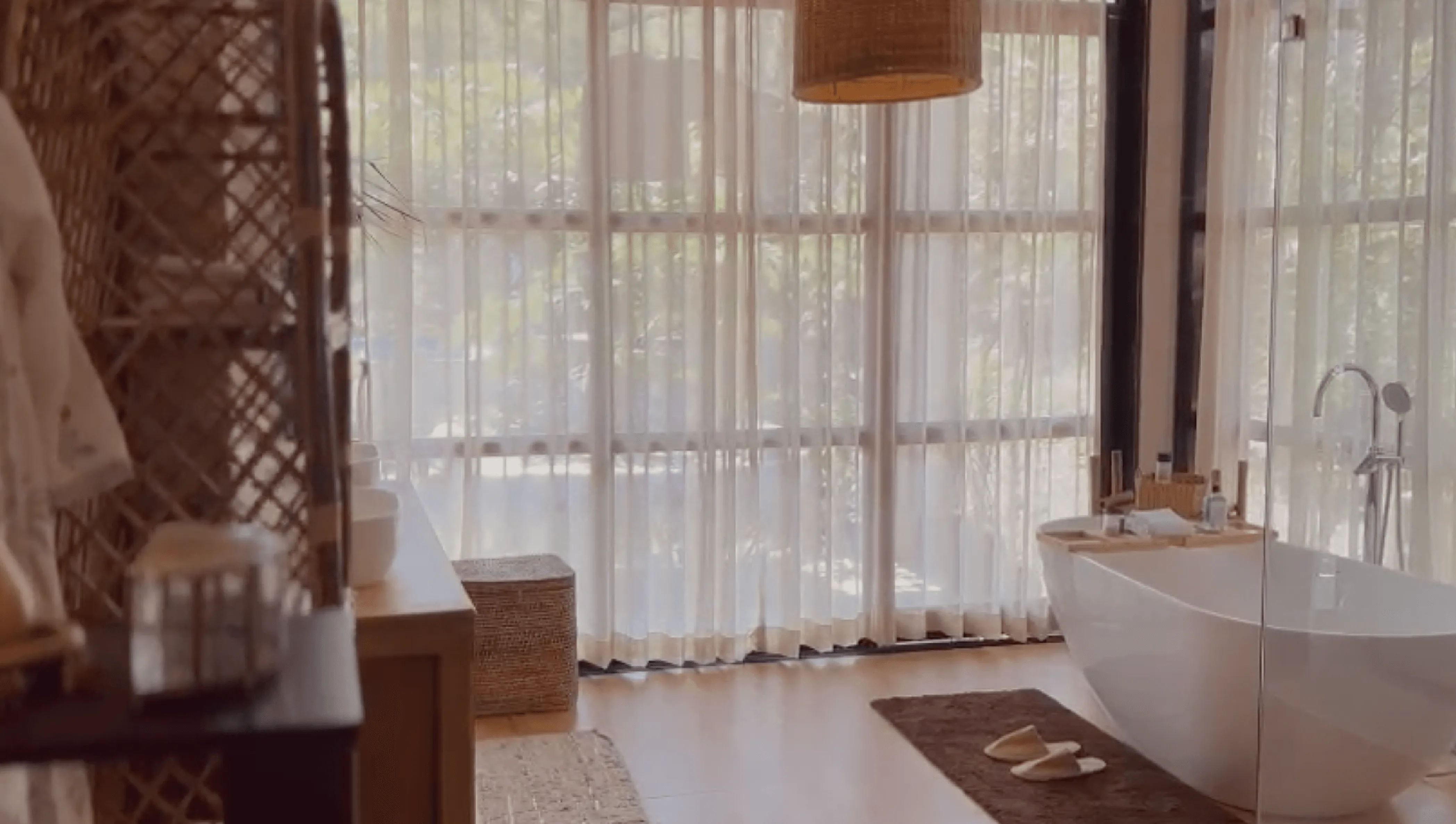 Luxurious boho-style bathroom with a freestanding bathtub, floor-to-ceiling sheer curtains, and natural rattan decor in Dhyaana Farms the Luxury Farmstay hotel in Aurangabad.