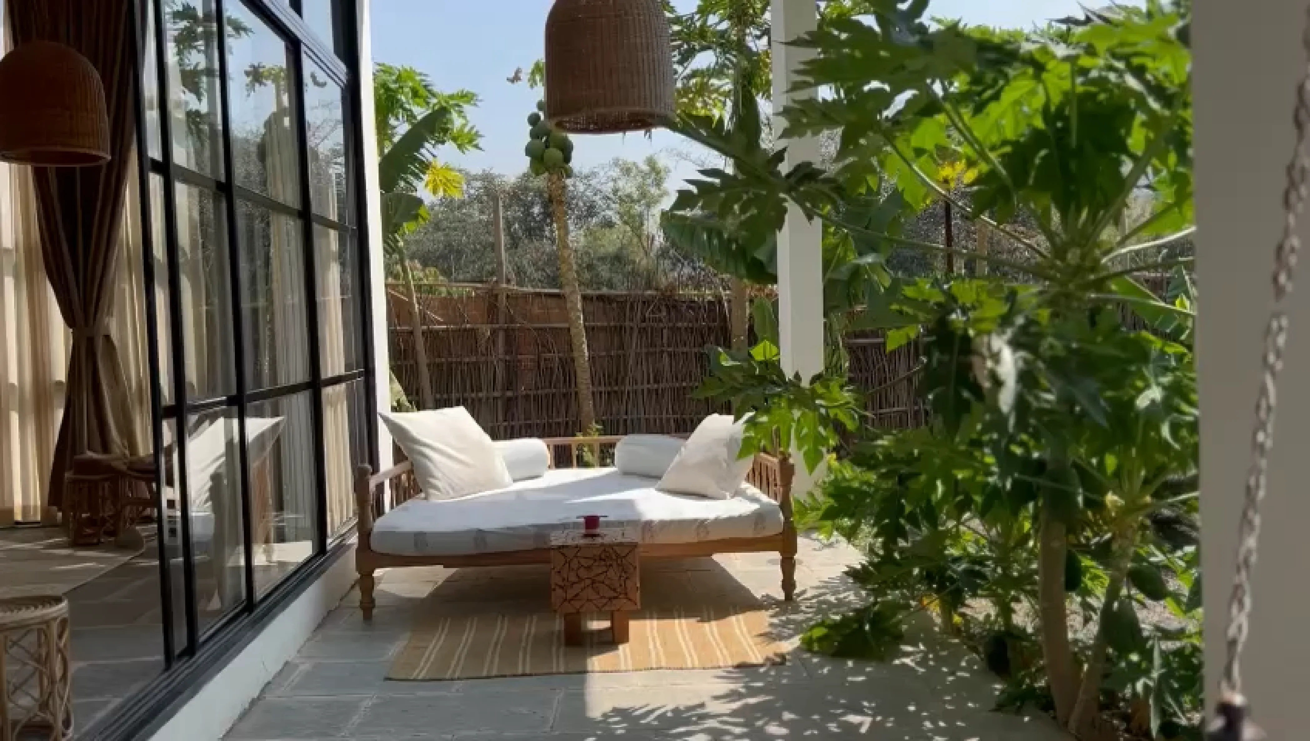 Tranquil outdoor lounge area with a wooden daybed, plush white cushions, and lush greenery, creating a tropical retreat in Dhyaana Farms