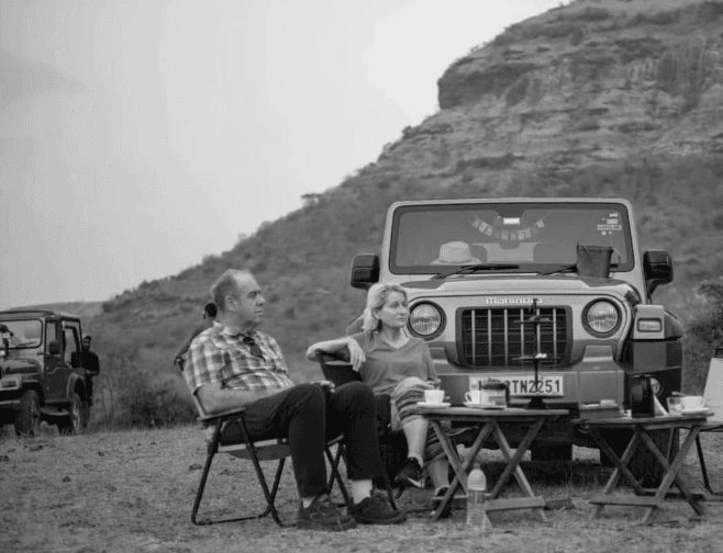 A couple enjoying an outdoor tea break beside their off-road vehicle in a mountainous landscape experiencing with Dhyaana Farms