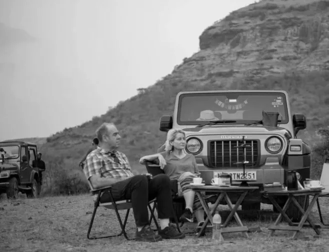 A couple enjoying an outdoor tea break beside their off-road vehicle in a mountainous landscape experiencing with Dhyaana Farms