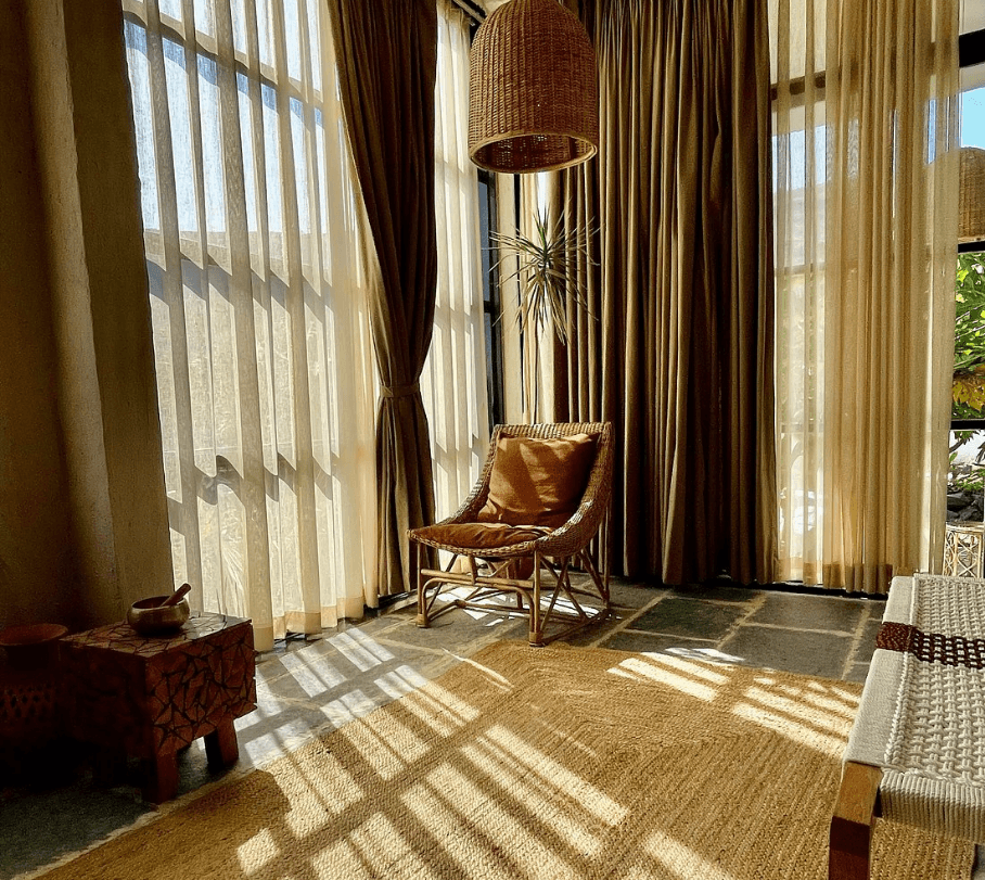 Cozy sunlit corner with a rattan chair, warm-toned curtains, and natural decor, creating a peaceful and inviting ambiance. Boutique Farmstay with Dhyaana Farms