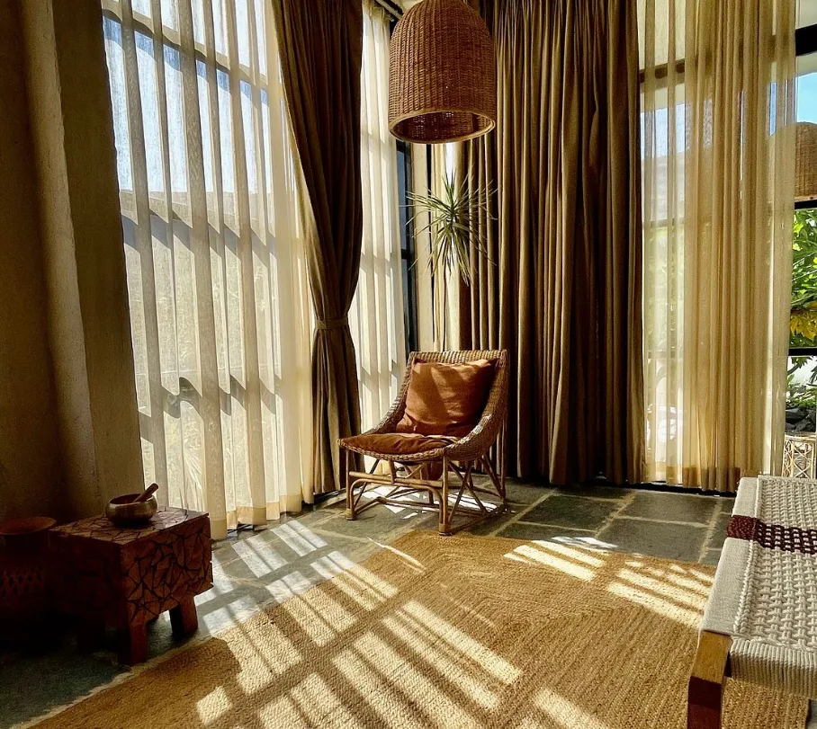Cozy sunlit corner with a rattan chair, warm-toned curtains, and natural decor, creating a peaceful and inviting ambiance. Boutique Farmstay with Dhyaana Farms