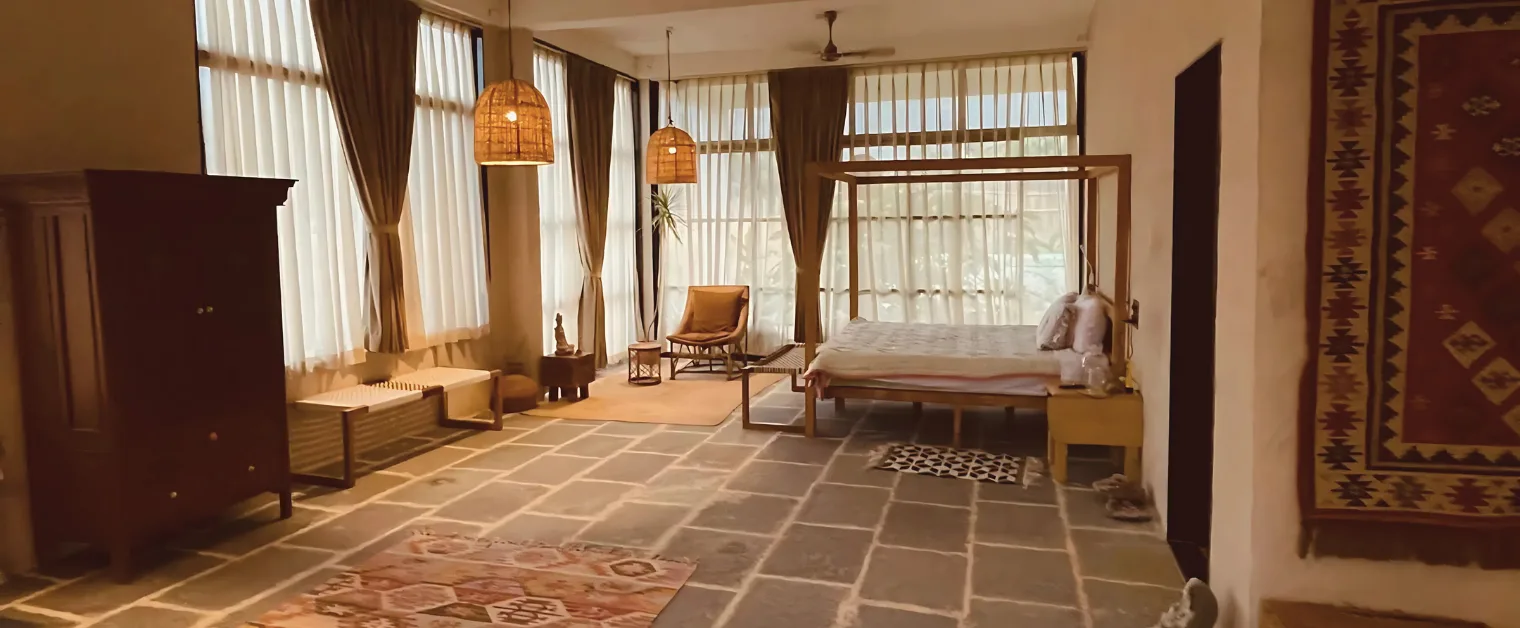 Spacious bohemian bedroom with a four-poster bed, earthy decor, large windows, and warm ambient lighting for a cozy retreat. Best Farm stay in Aurangabad