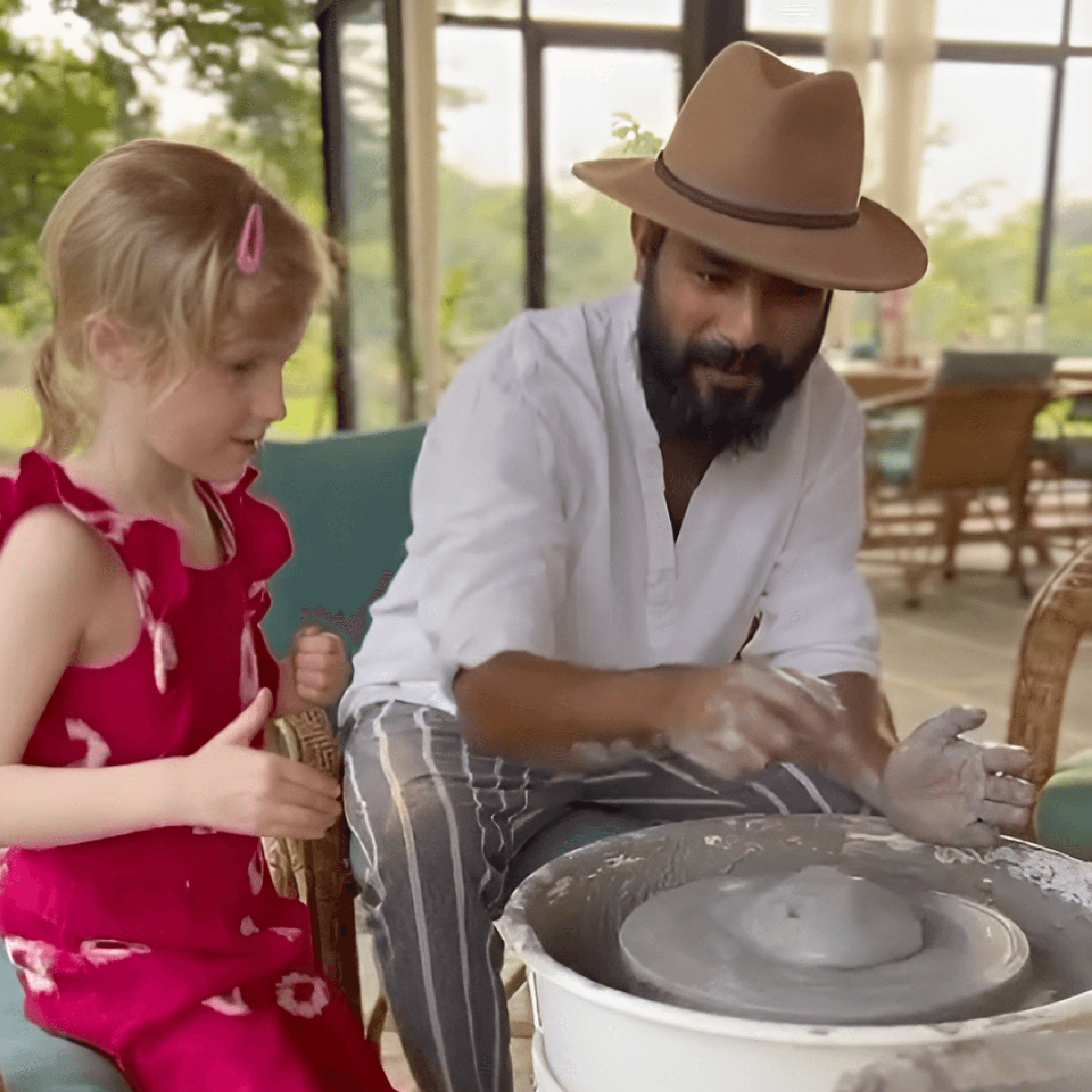 Man teaching pottery to a young girl in a pottery workshop inside the Farm.