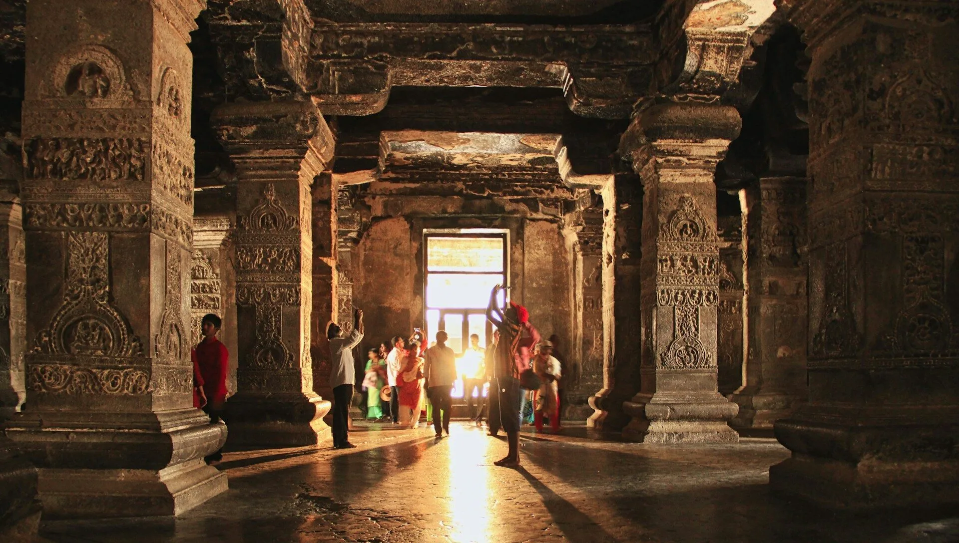 Sunlight pours into an ancient Kailasa Temple, highlighting carved pillars and visitors